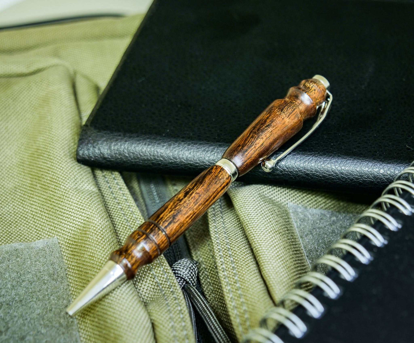 Handmade twist pen made of desert ironwood with chrome hardware on fabric and notebook background
