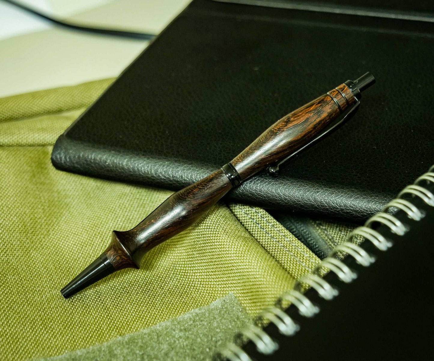 Handmade ebony wood click pen with black chrome accents resting on fabric and notebooks
