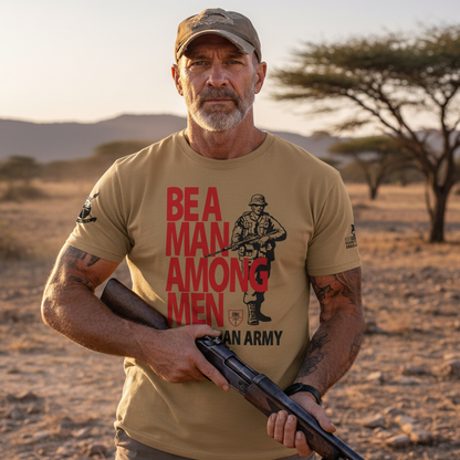 Man wearing a tan “Be a Man Among Men” Rhodesian Army graphic T-shirt in an outdoor African-style landscape, shown in a lifestyle setting with rugged terrain and trees in the background.